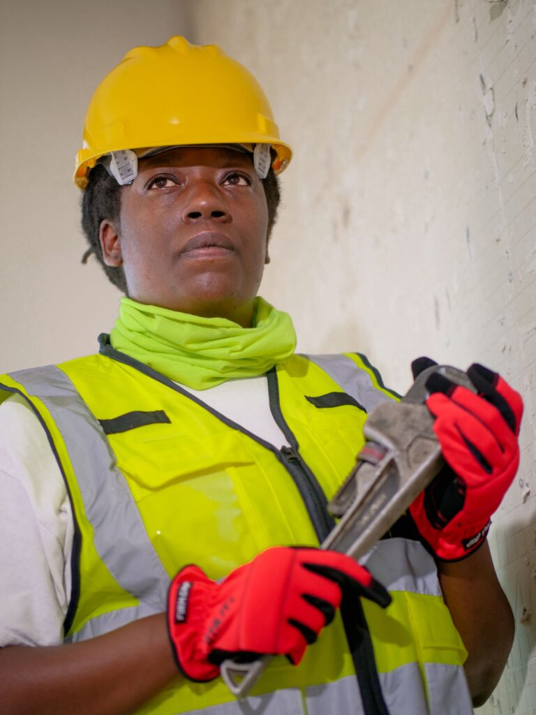 A professional female plumber wearing protective gear, ready for work indoors.